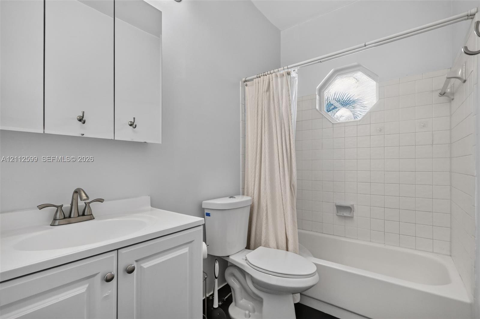 Bathroom featuring a vanity cabinet with integrated countertop, octagonal window, white ceramic tile tub surround, and a wall-mounted mirrored medicine cabinet