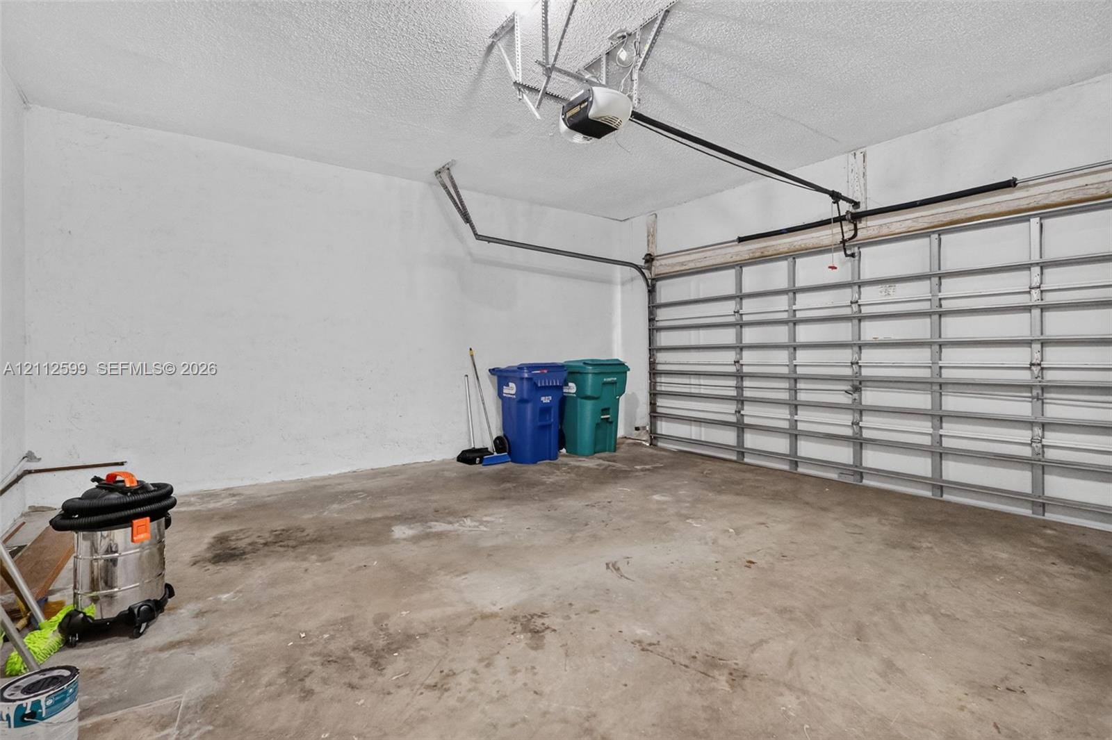 Enclosed garage featuring a concrete floor, textured ceiling, and automatic sectional garage door opener