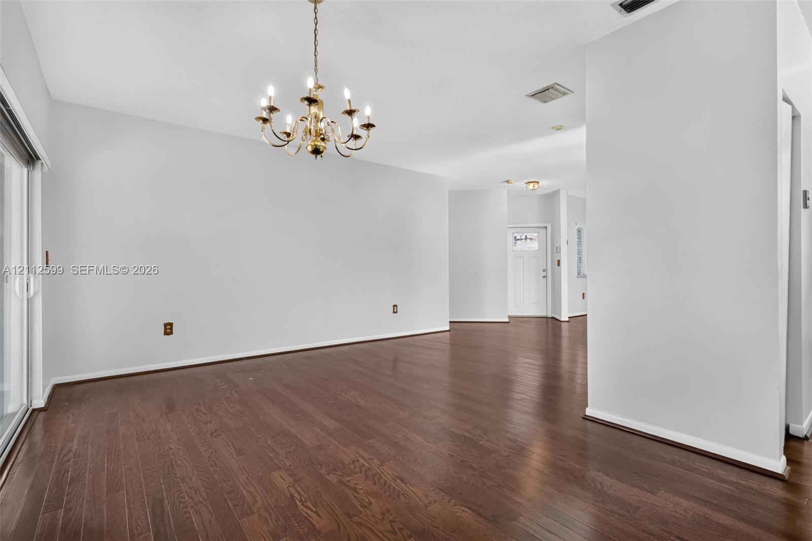 Open-concept interior featuring wood-finish flooring, a multi-arm chandelier, and sliding glass doors