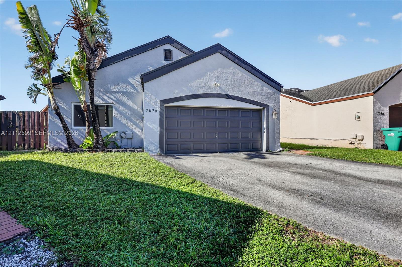Stucco exterior with an arched entryway, single-car garage, asphalt driveway, and mature landscaping