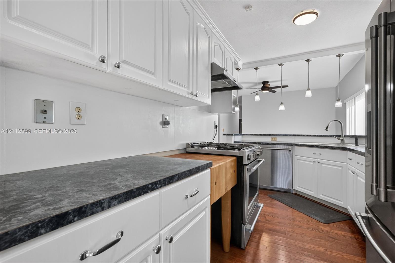 Kitchen featuring white cabinetry, dark countertops, integrated butcher-block prep station, stainless steel appliances, and wood-finish flooring