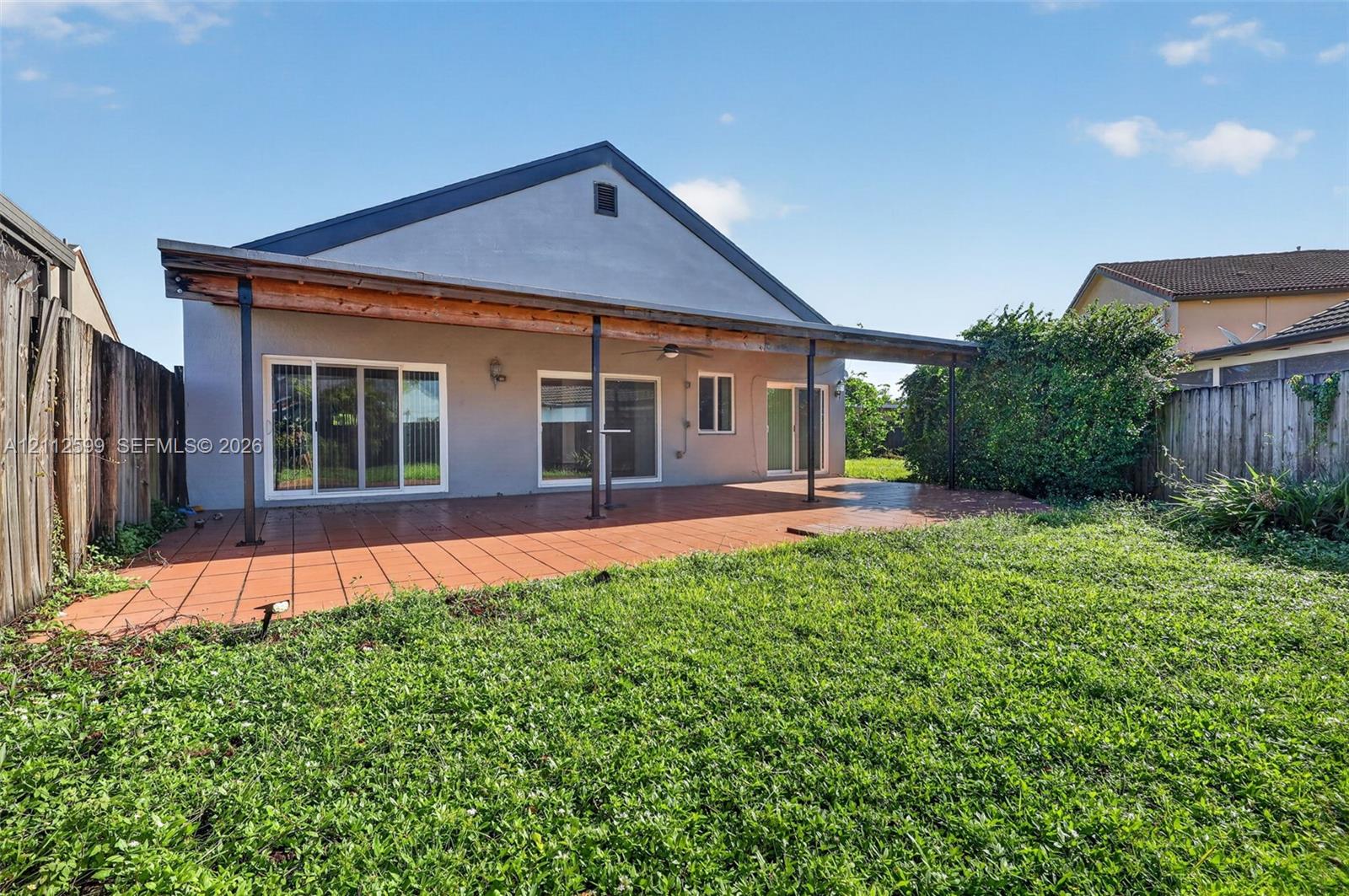 Rear exterior featuring a covered patio with tile flooring, three sliding glass doors, and a wood-beam support structure
