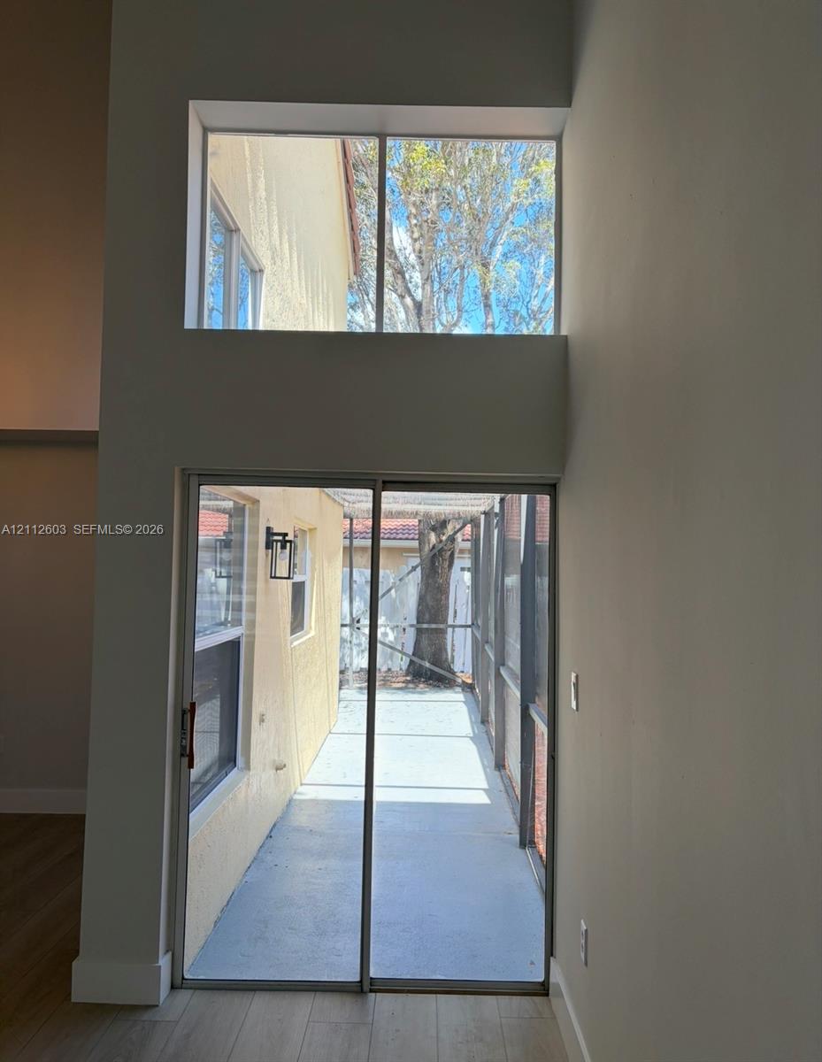 Double-height wall featuring a sliding glass door and an upper transom window, wood-finish flooring, and a screened-in patio area Double-height wall featuring a sliding glass door and an upper transom window, wood-finish flooring, and a screened-in patio area
