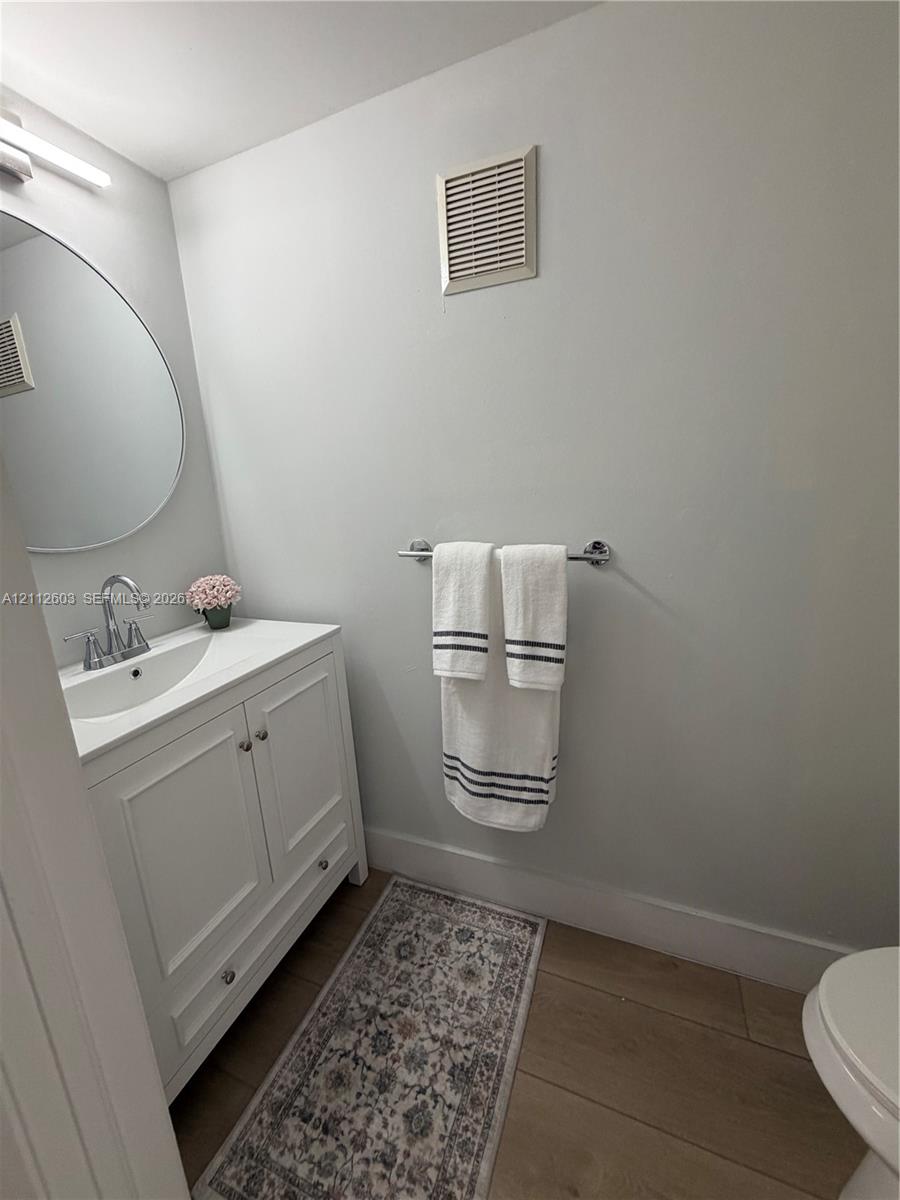 Guest Bathroom. Brand new white cabinetry vanity with a polished chrome faucet, round wall mirror, and wood-finish flooring