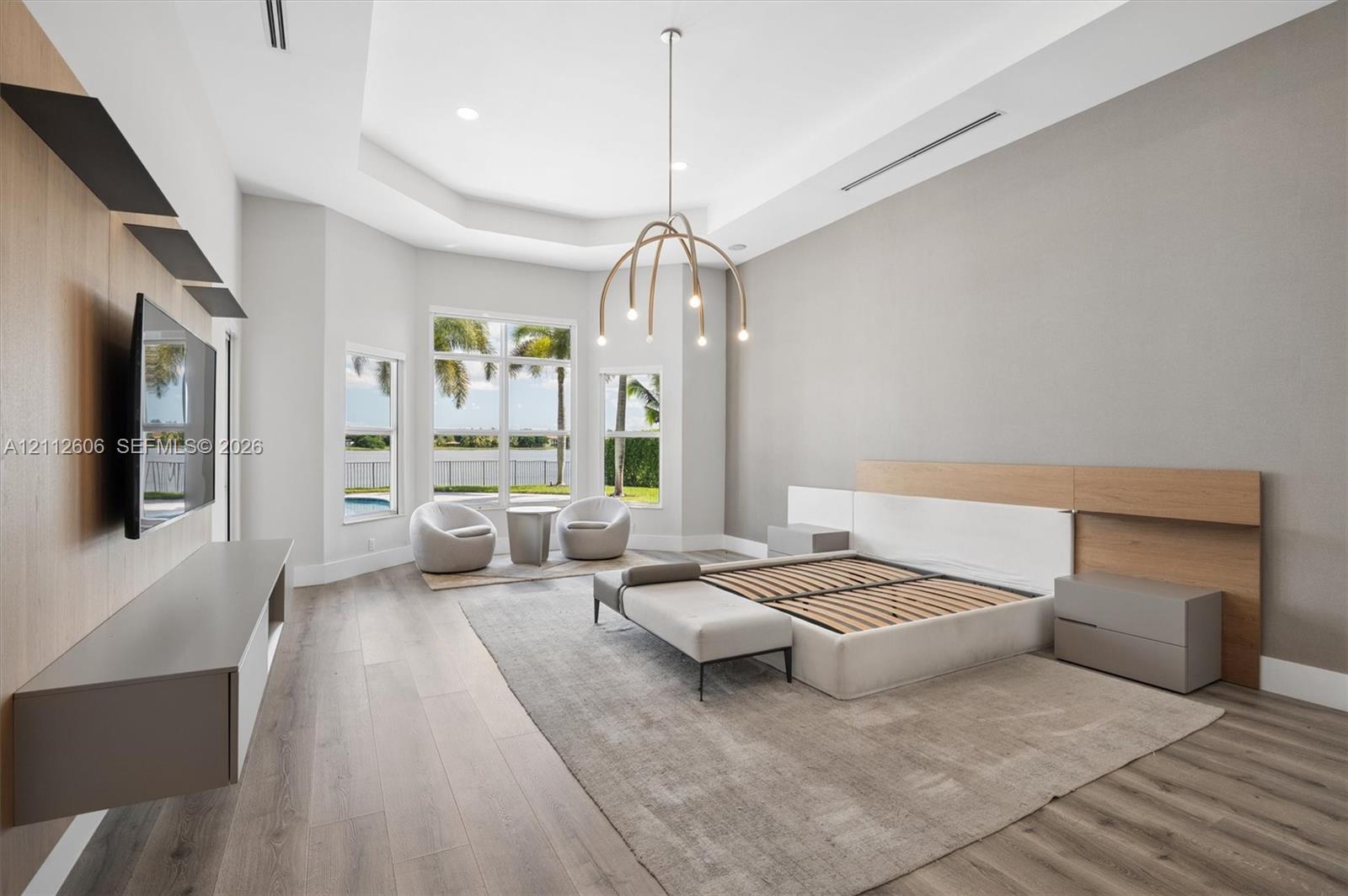 Tray ceiling featuring recessed lighting, wood-finish flooring, built-in wall-mounted cabinetry, custom wood-paneled headboard, and expansive windows with water scenery
