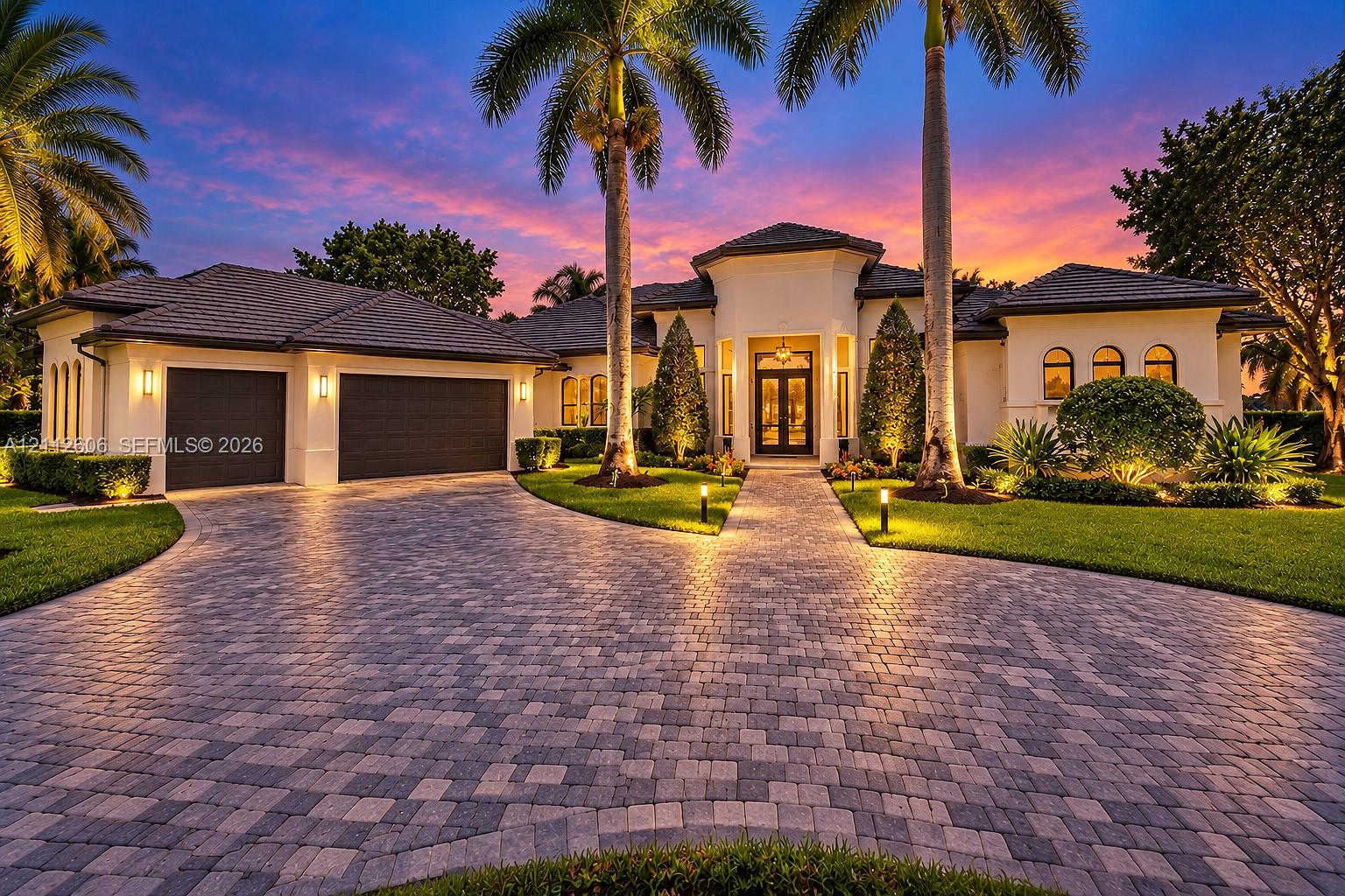Stucco exterior featuring a multi-gabled tile roof, paver driveway, double-door entryway, and integrated landscape lighting