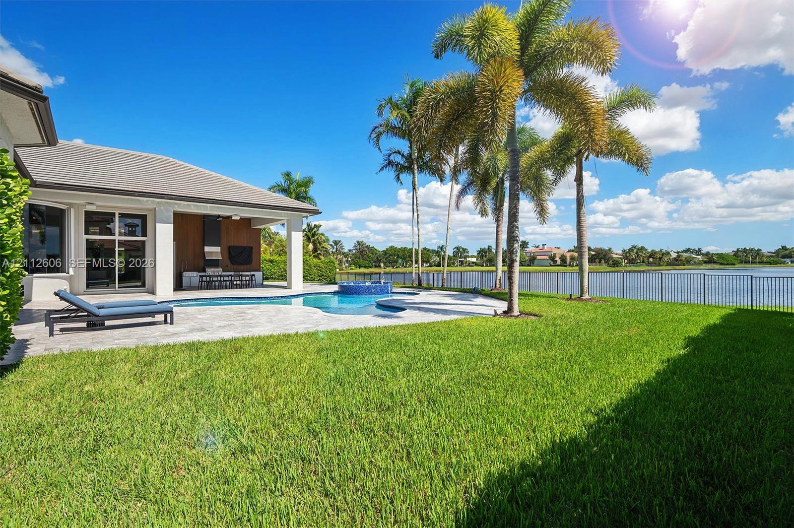Rear exterior featuring a covered patio, paved pool deck, swimming pool with integrated spa, manicured lawn, and water frontage