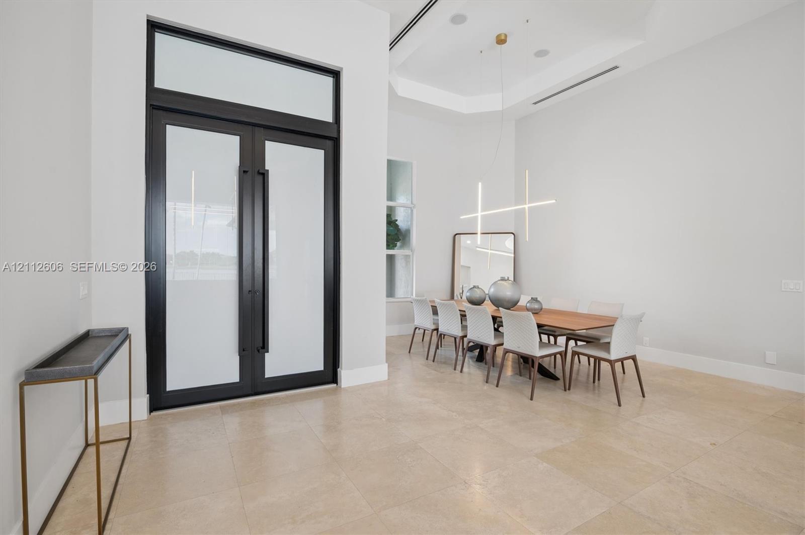 Double-door entryway featuring frosted glass panels and a transom window, complemented by large-format tile flooring, a tray ceiling, and a linear pendant light fixture