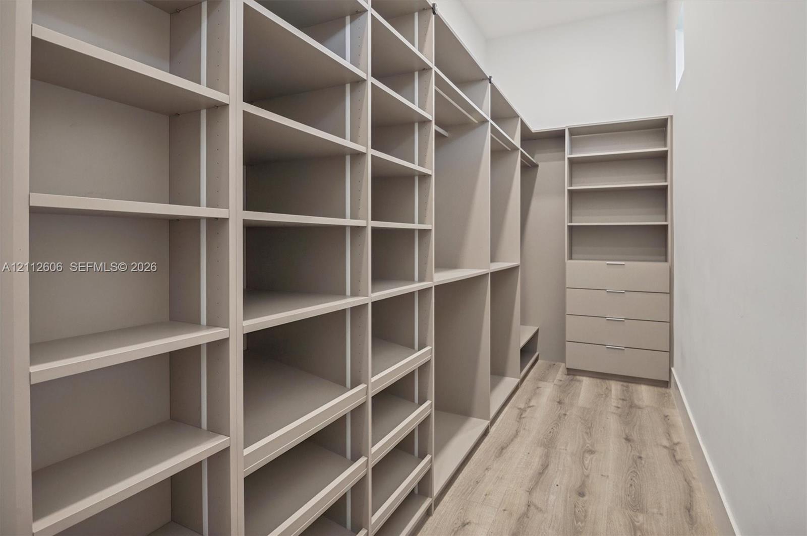 Custom floor-to-ceiling cabinetry, integrated shelving units, dedicated hanging rods, built-in soft-close drawers, and wood-finish flooring