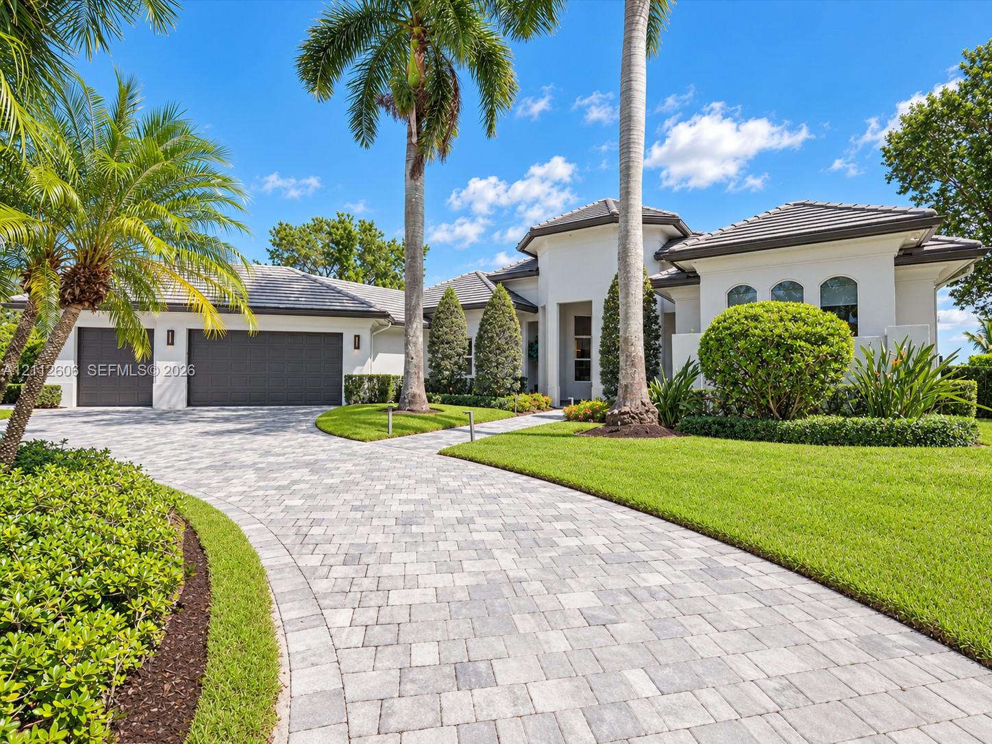 Stucco exterior featuring a multi-car garage, concrete tile roof, paver driveway, and professional landscaping