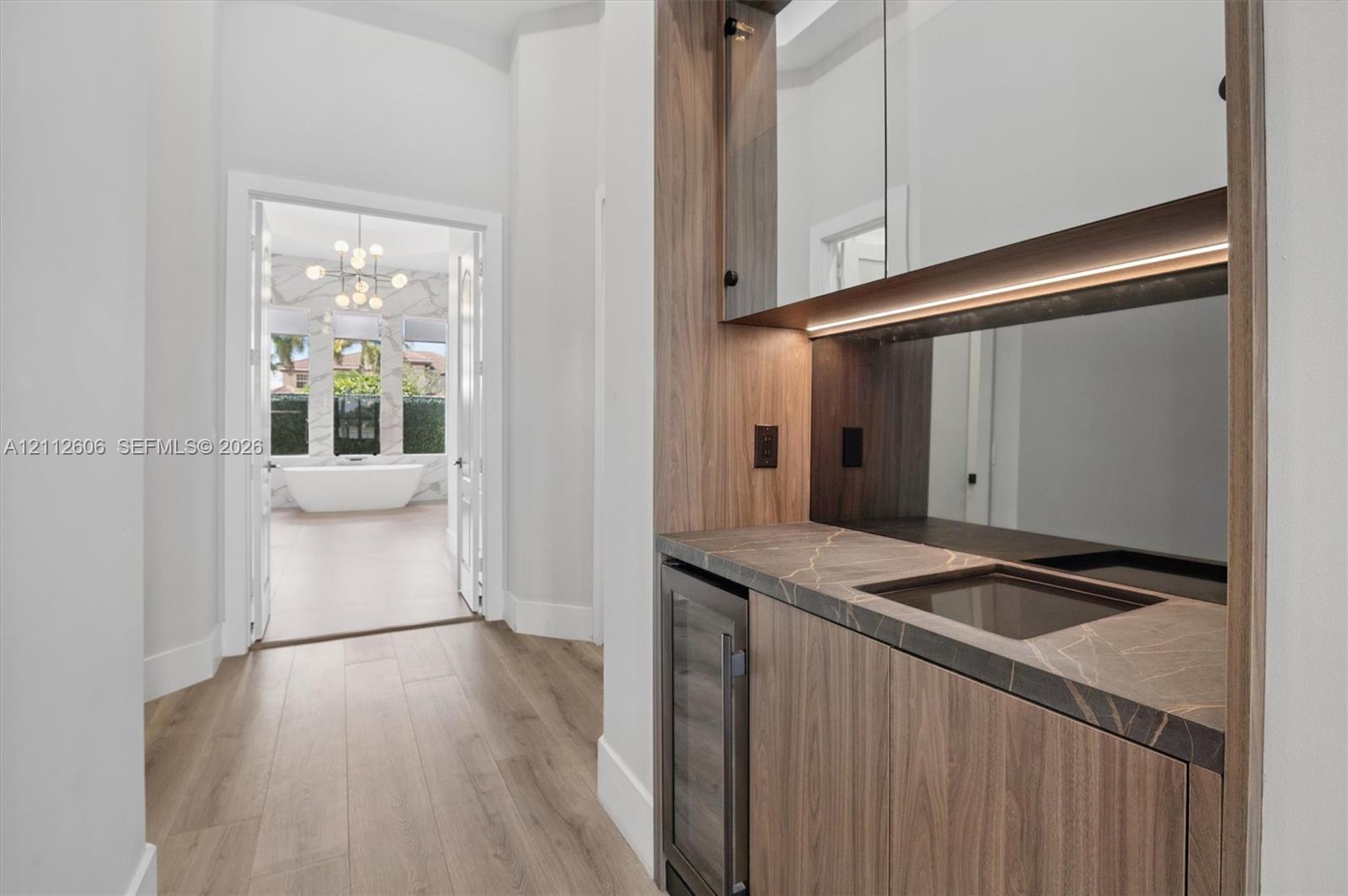 Custom cabinetry featuring wood-finish cabinetry, a stone countertop with integrated sink, built-in beverage refrigerator, under-cabinet lighting, and wood-finish flooring