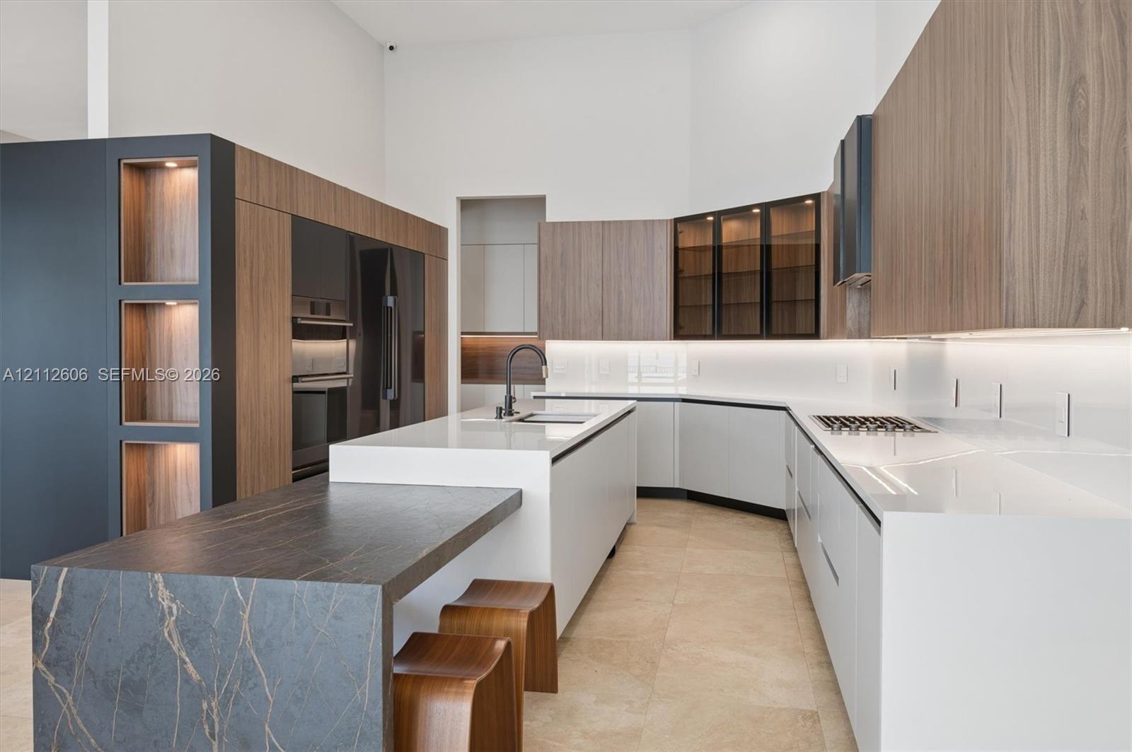 Kitchen featuring white solid-surface countertops, wood-finish cabinetry, a large stone-topped kitchen island, built-in wall ovens, and under-cabinet integrated lighting