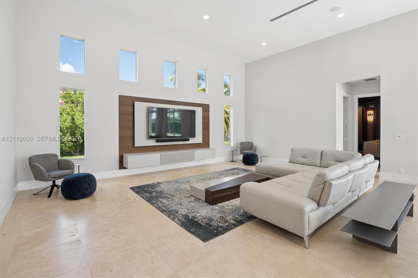 High-ceilinged living area featuring stone flooring, integrated wood-paneled media wall, wall-mounted floating cabinetry, and floor-to-ceiling vertical windows