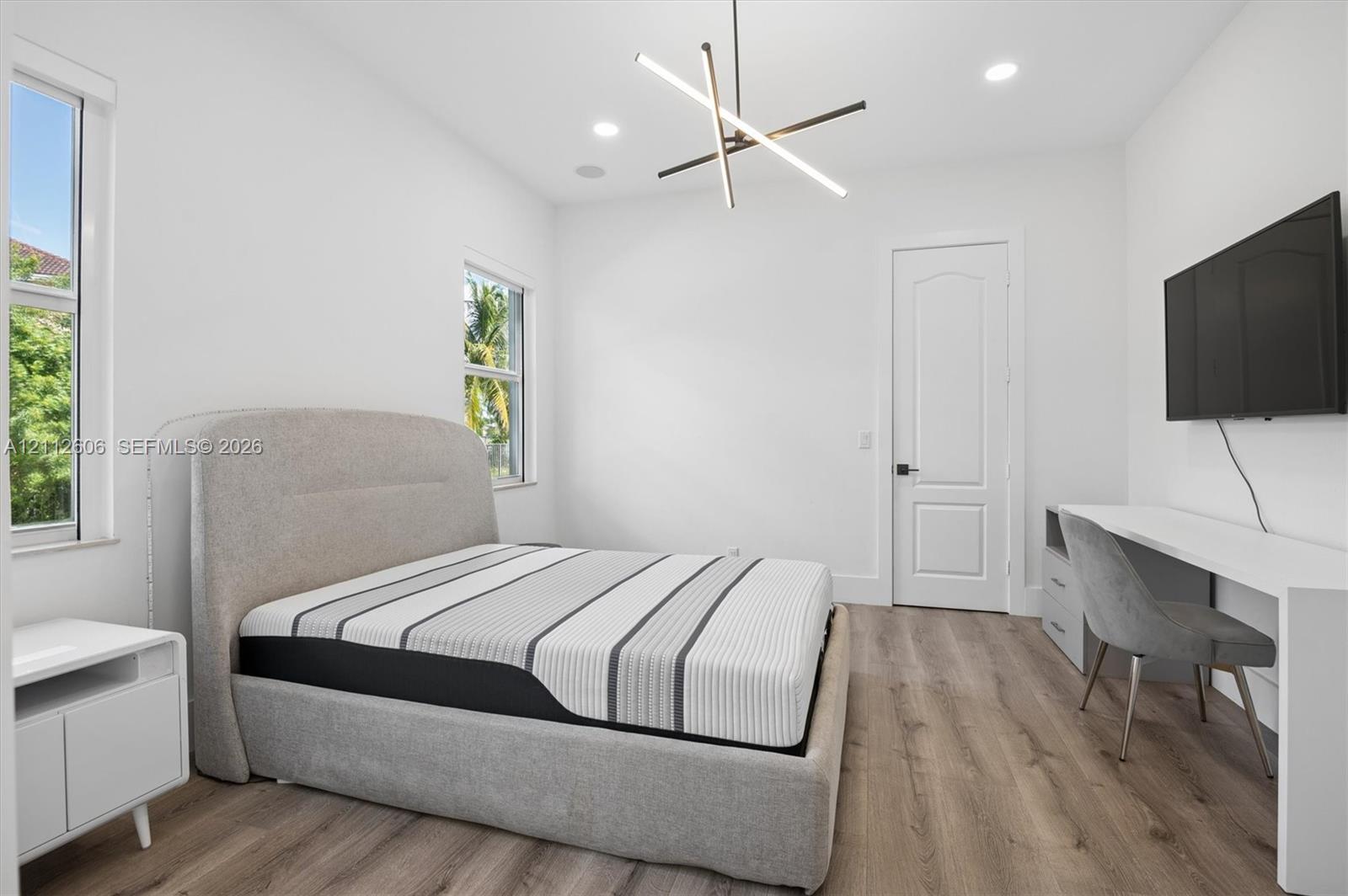 Wood-finish flooring, geometric architectural light fixture, recessed ceiling lighting, and multi-panel interior door