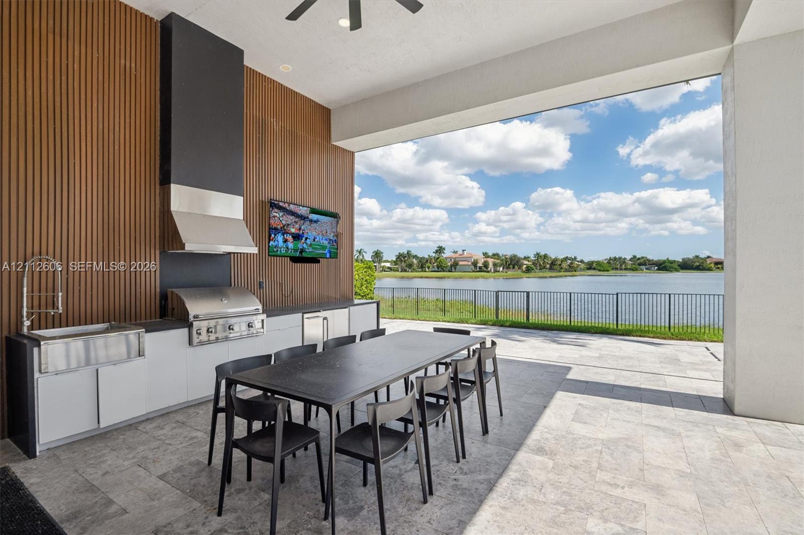 Covered outdoor kitchen featuring a stainless steel grill, farm-style sink, slate-toned cabinetry, vertical wood-slat accent wall, and stone paver flooring