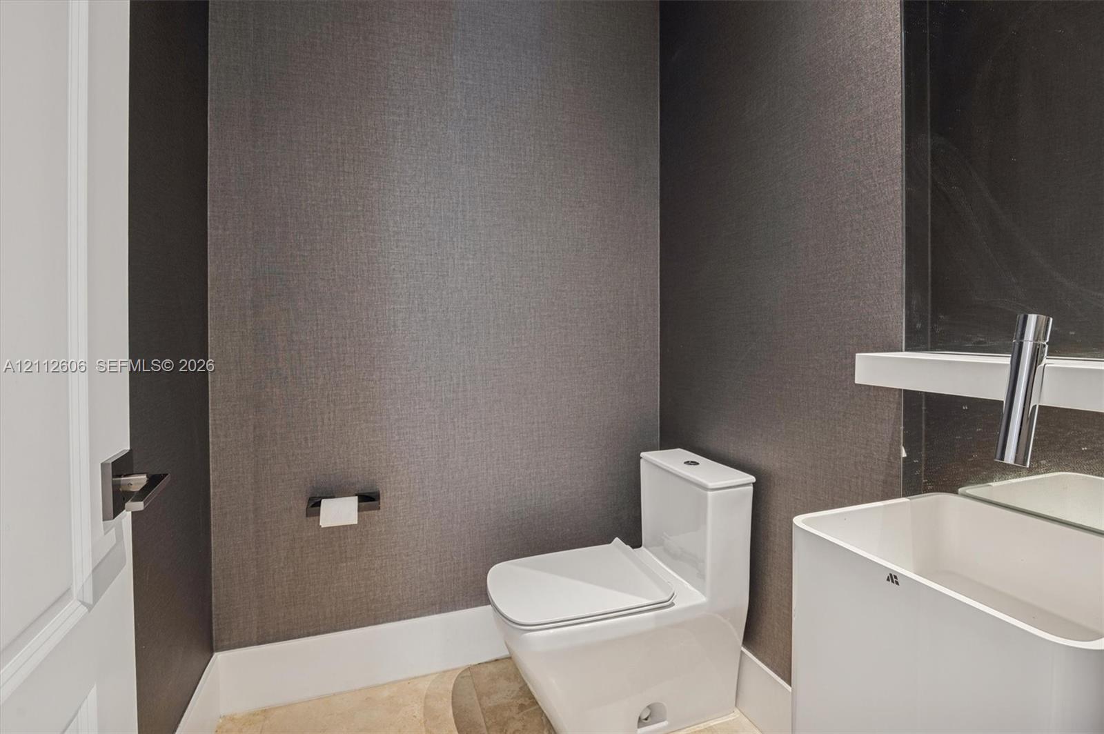 Textured charcoal wall covering, minimalist white vessel sink, wall-mounted faucet, and polished floor tile