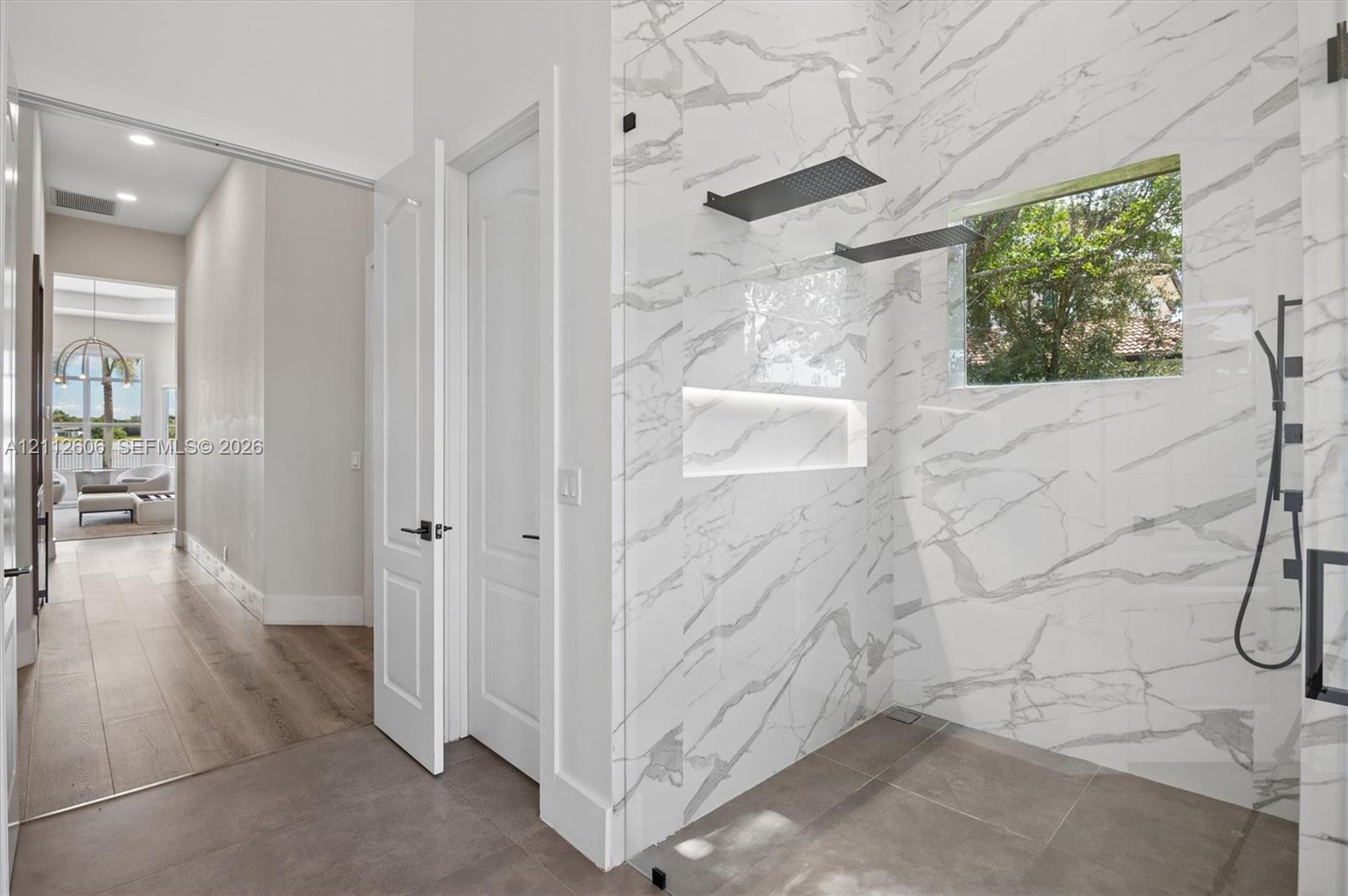 Walk-in shower featuring floor-to-ceiling stone-patterned tile, a recessed niche, black matte hardware, and an integrated glass enclosure, complemented by large-format tile flooring
