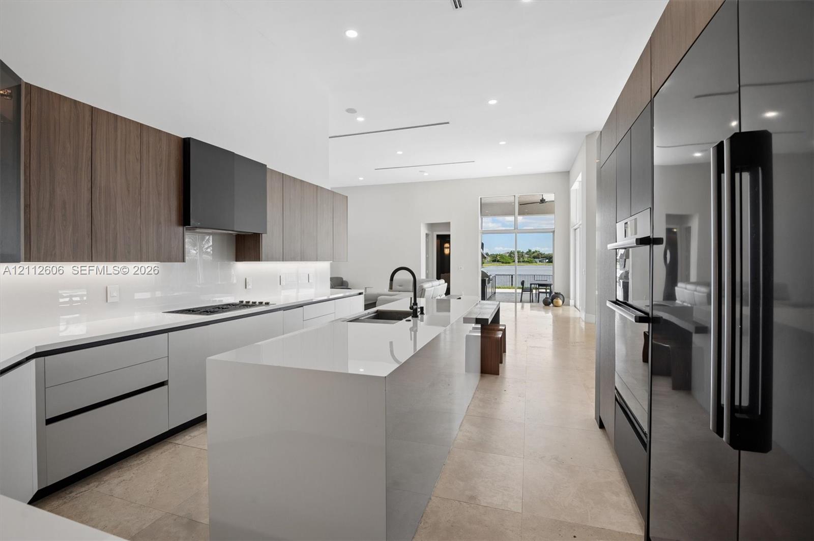 Modern kitchen featuring a waterfall-edge center island, quartz countertops, flat-panel cabinetry, integrated appliances, and stone-finish flooring