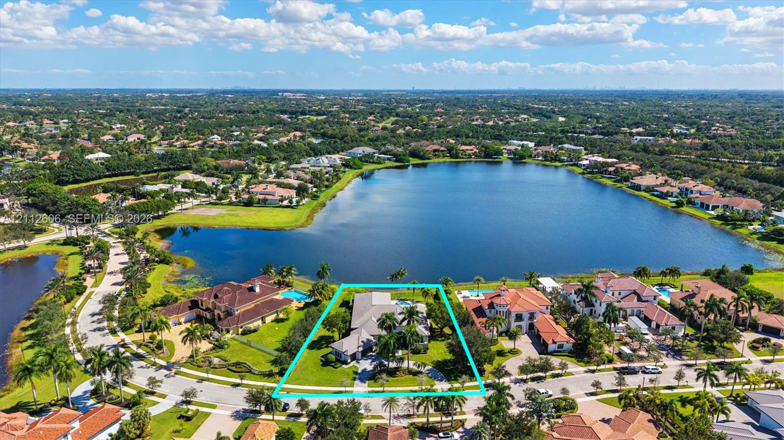 Aerial perspective of a waterfront property featuring a paved driveway, multi-car garage, expansive green space, and an integrated swimming pool
