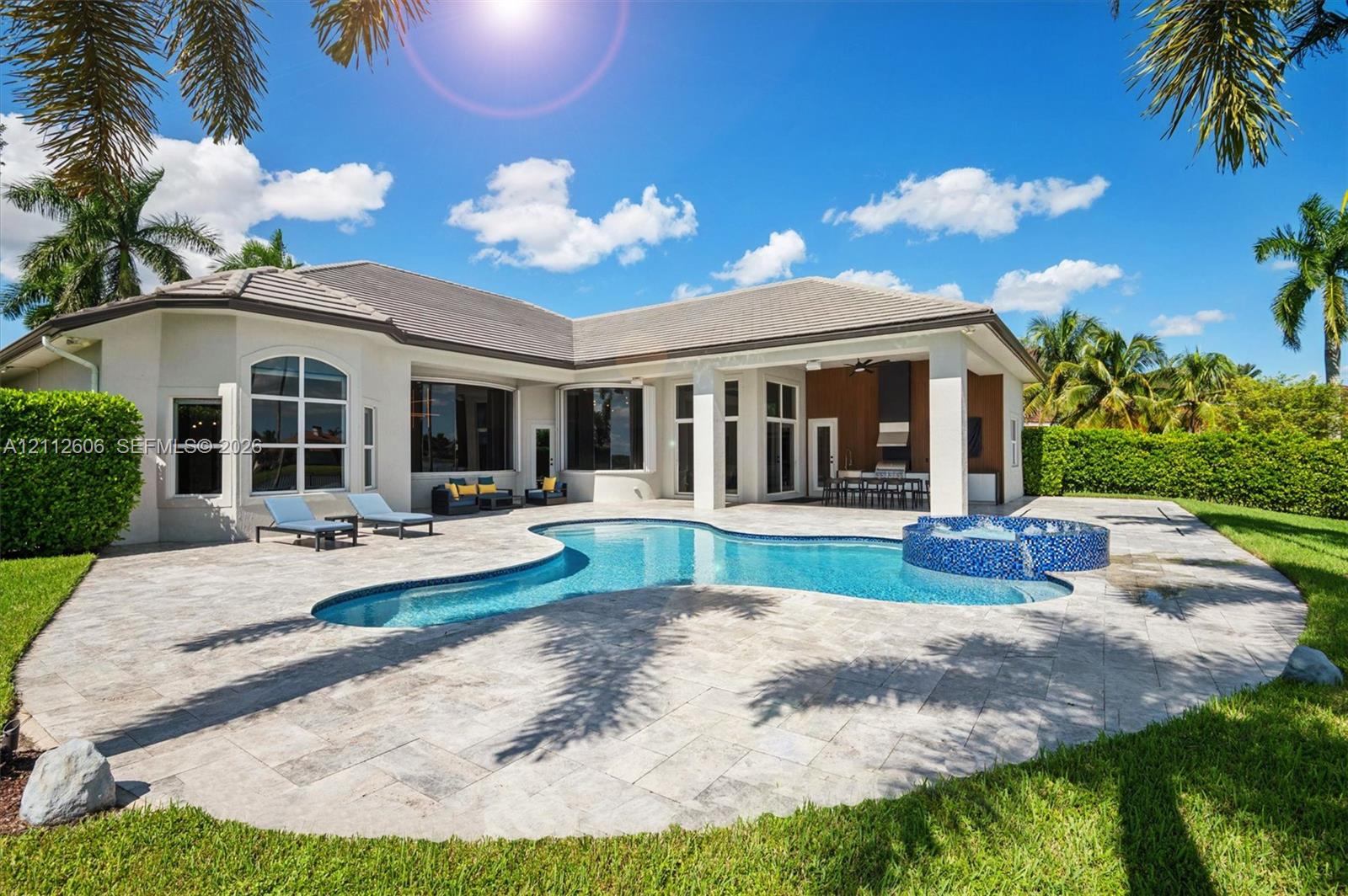 Custom-shaped swimming pool with an integrated tiled spa, expansive stone-paver patio, and covered outdoor kitchen area