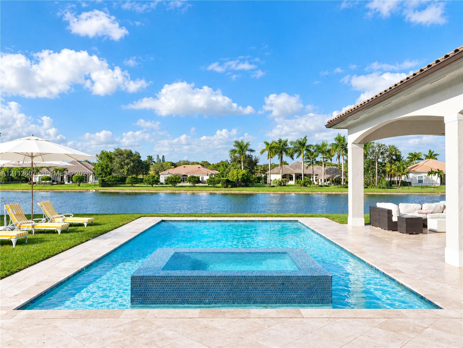 Rectangular swimming pool with an integrated tile-finished spa, expansive stone-paver deck, covered lanai, and waterfront positioning