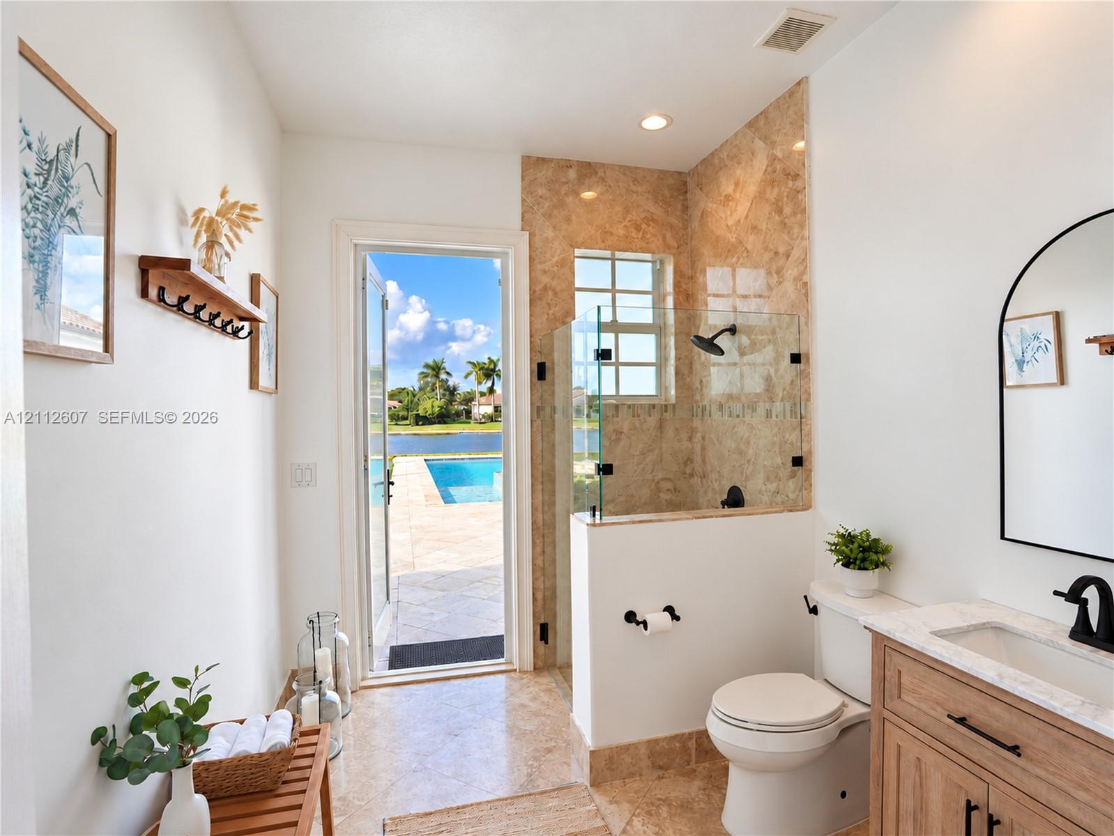 Bathroom featuring a walk-in shower with stone tile surround, glass enclosure, and matte black fixtures, paired with a wood-finish vanity topped with a stone countertop