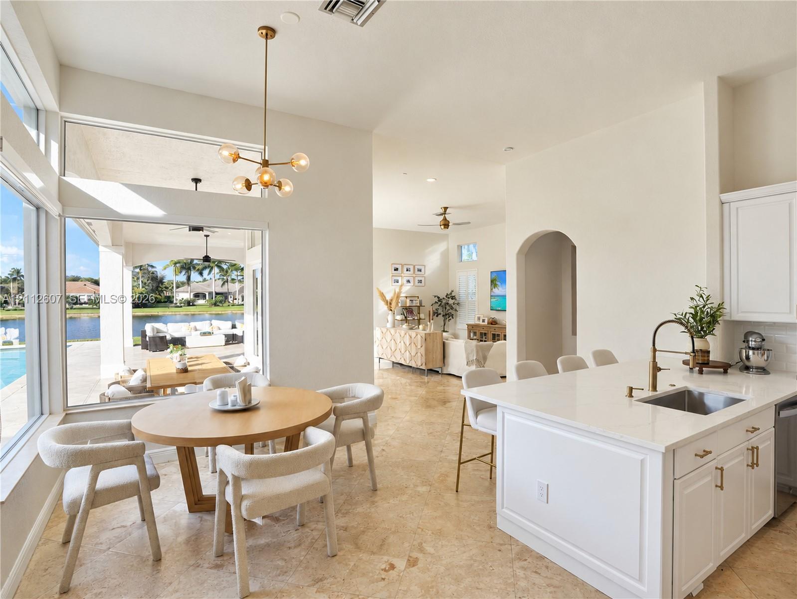 Open-concept kitchen featuring an island with stone-surface countertop, undermount sink, and metallic faucet hardware, complemented by natural stone flooring and a multi-light pendant fixture