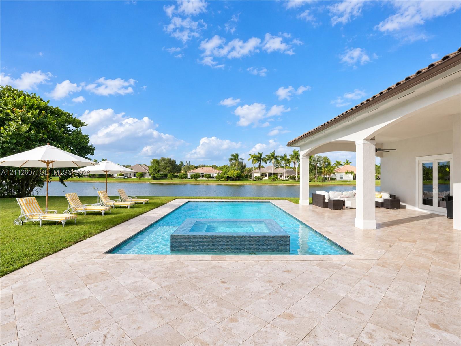 Covered patio with natural stone flooring, swimming pool featuring an integrated spa, and lawn area with water frontage