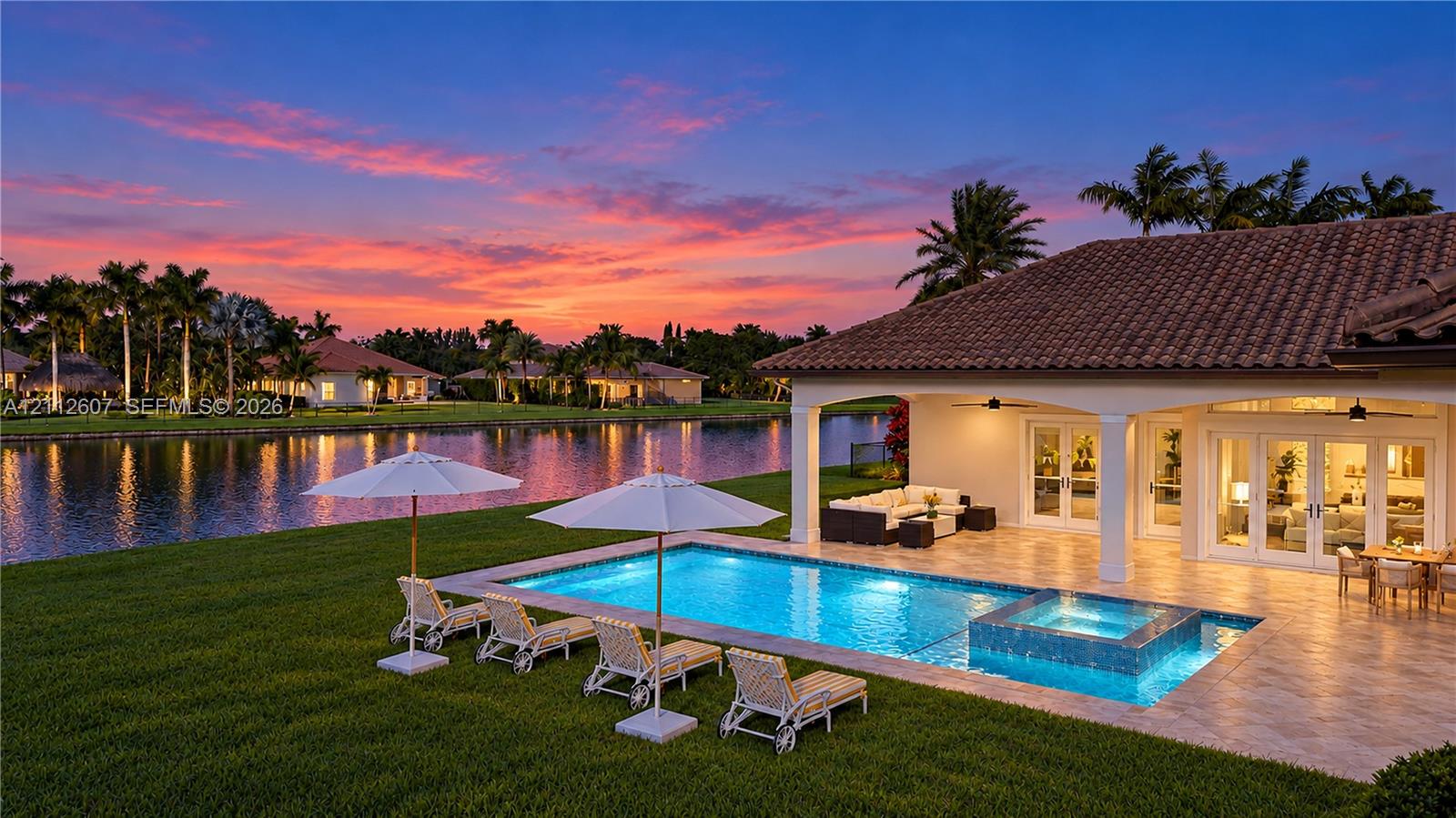 Waterfront outdoor space featuring a covered tile patio, a built-in swimming pool with a raised spa, and manicured landscaping Waterfront outdoor space featuring a covered tile patio, a built-in swimming pool with a raised spa, and manicured landscaping