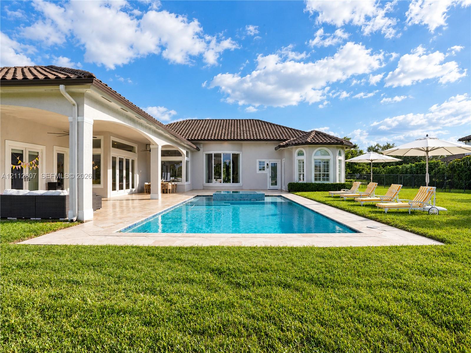 Stucco exterior with a tiled roof featuring a covered lanai, inground pool with an integrated spa, and expansive lawn