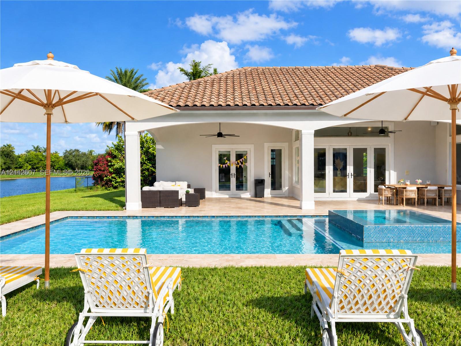 Covered patio with a tile roof, rectangular swimming pool with an integrated spa, and limestone paver decking