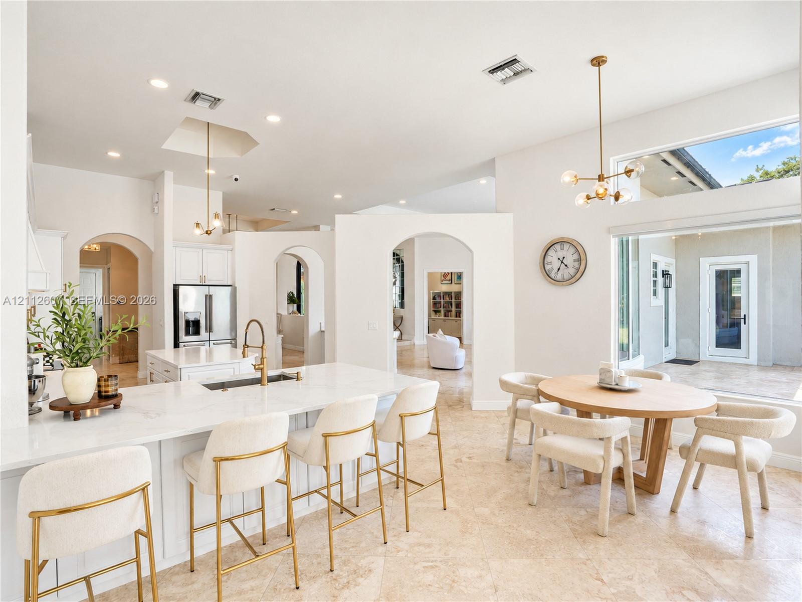 Open-concept interior featuring high ceilings, stone flooring, a center island with stone countertop, brass-finish pendant lighting, and arched architectural openings