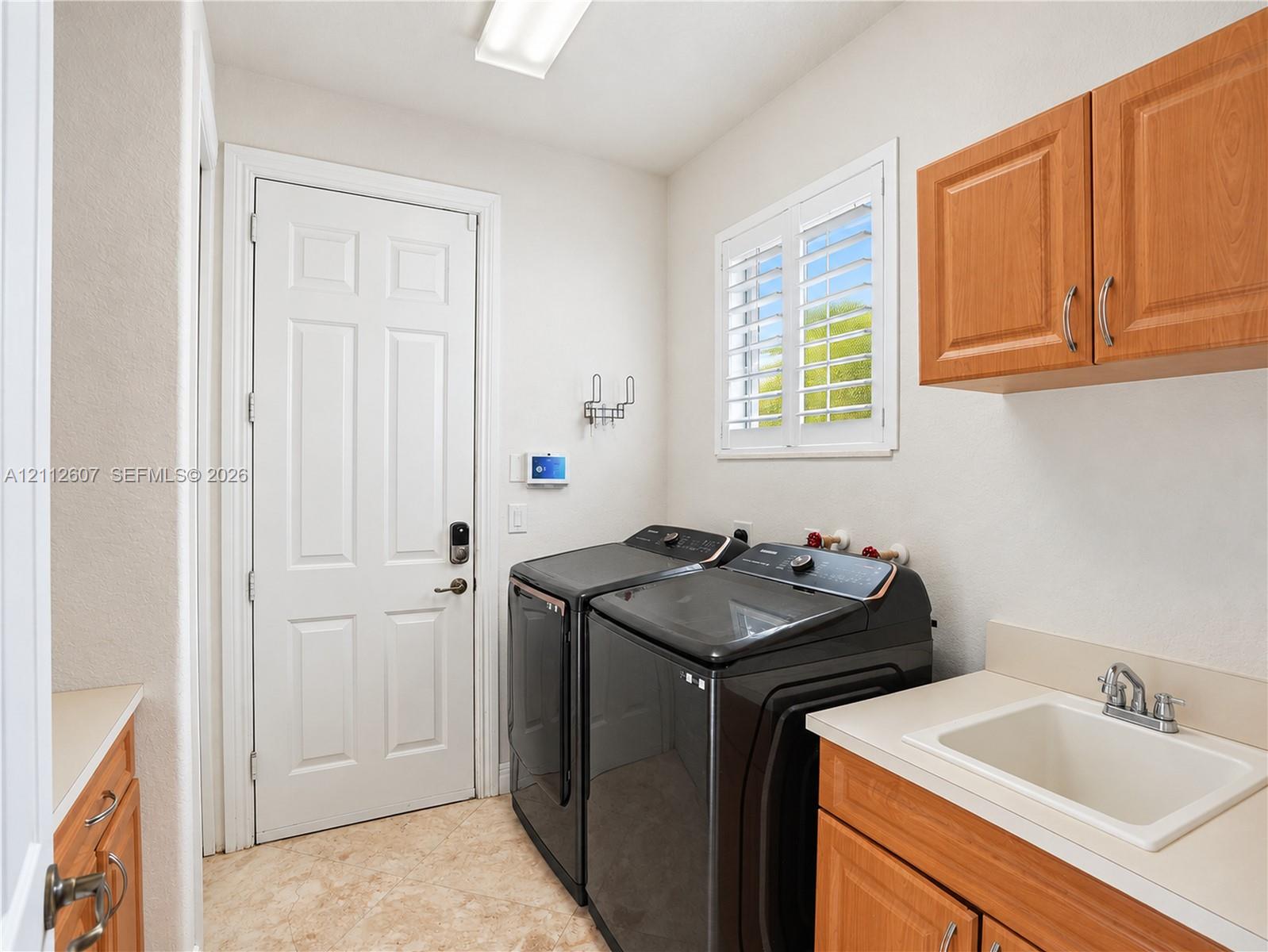 Utility room featuring wood-finish cabinetry, a drop-in sink, stone-surface counters, and white plantation shutters