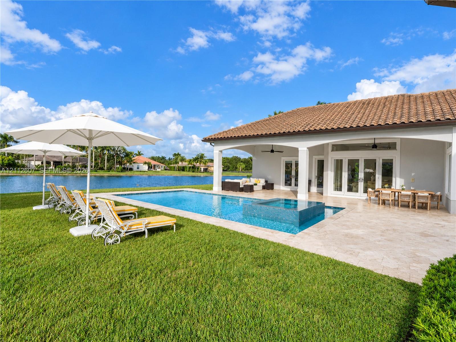 Covered patio with a tile roof, pool and integrated spa with stone tile surround, stone-paved deck, and water frontage