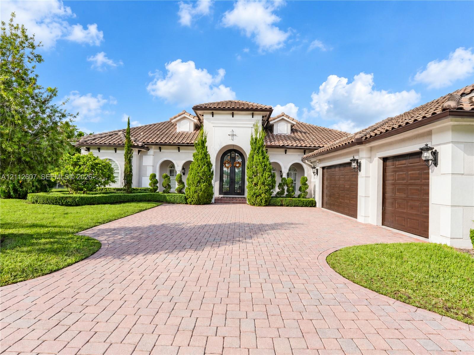 Mediterranean-style exterior featuring a paved stone driveway, arched entryways, tile roof, and multi-car garage with wood-finish doors