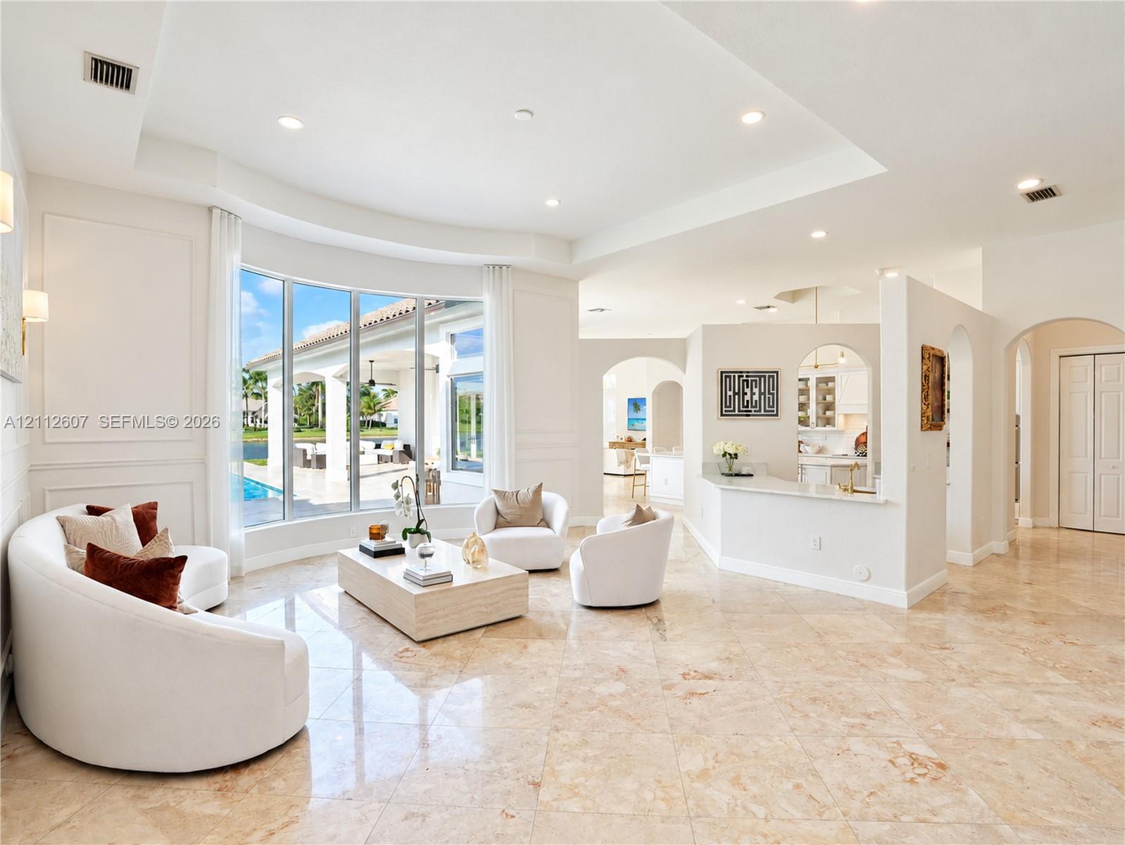 Spacious living area featuring polished stone flooring, a tray ceiling, curved bay windows, and a built-in partition wall with an integrated breakfast bar