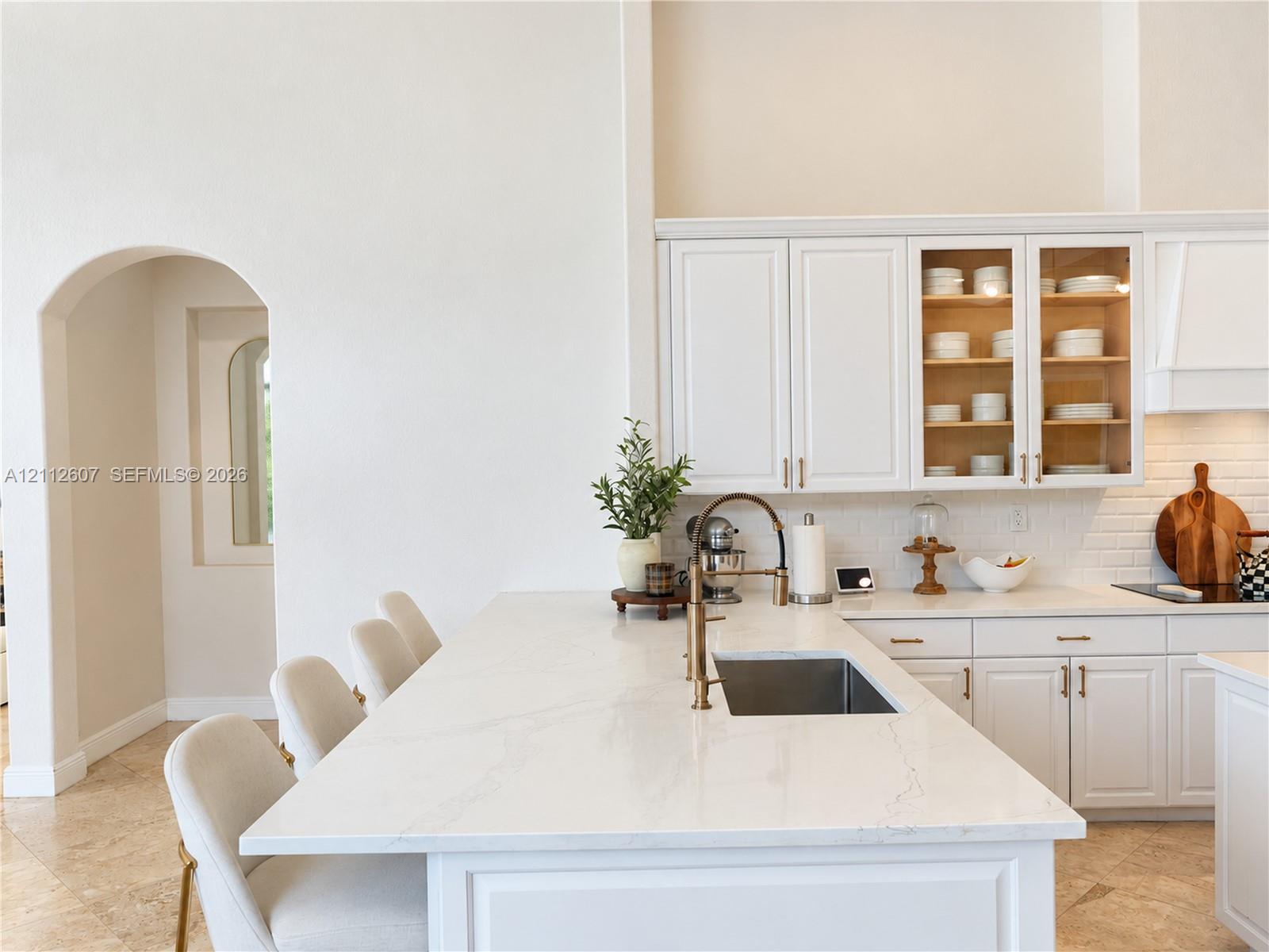Kitchen featuring white cabinetry, an expansive island with stone-finish countertops, subway tile backsplash, and an arched entry