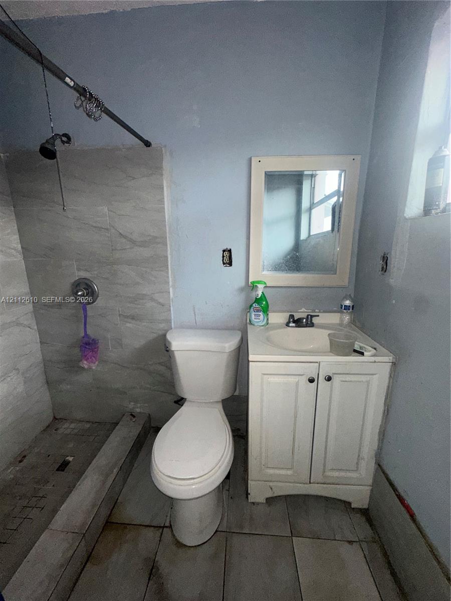 Bathroom featuring a tiled shower enclosure, a white vanity with an integrated sink, a wall-mounted mirror, and tile flooring
