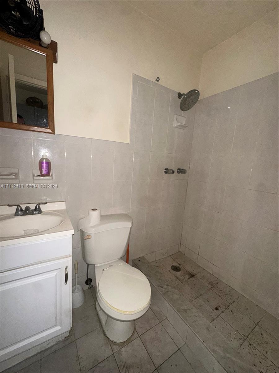 Bathroom featuring a white vanity cabinet, ceramic sink with chrome hardware, standard toilet, and a tiled shower stall with wall-mounted showerhead