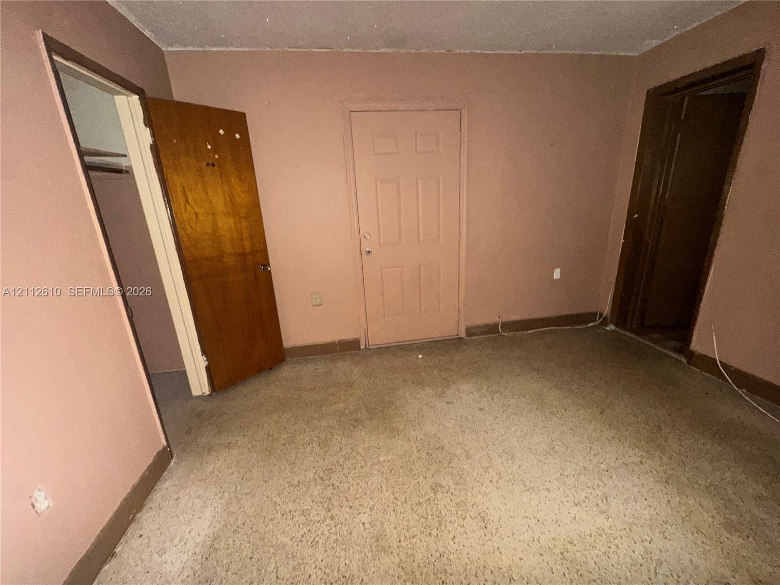 Interior room featuring neutral-toned wall paint, carpeted flooring, a six-panel door, and two entryways leading to separate spaces