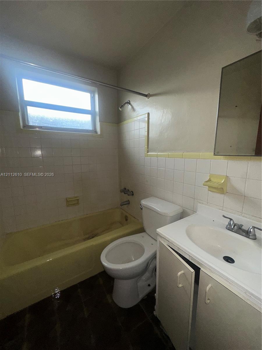 Bathroom featuring a built-in bathtub, a wall-mounted medicine cabinet, white tiled wall surrounds, and a vanity cabinet with an integrated sink