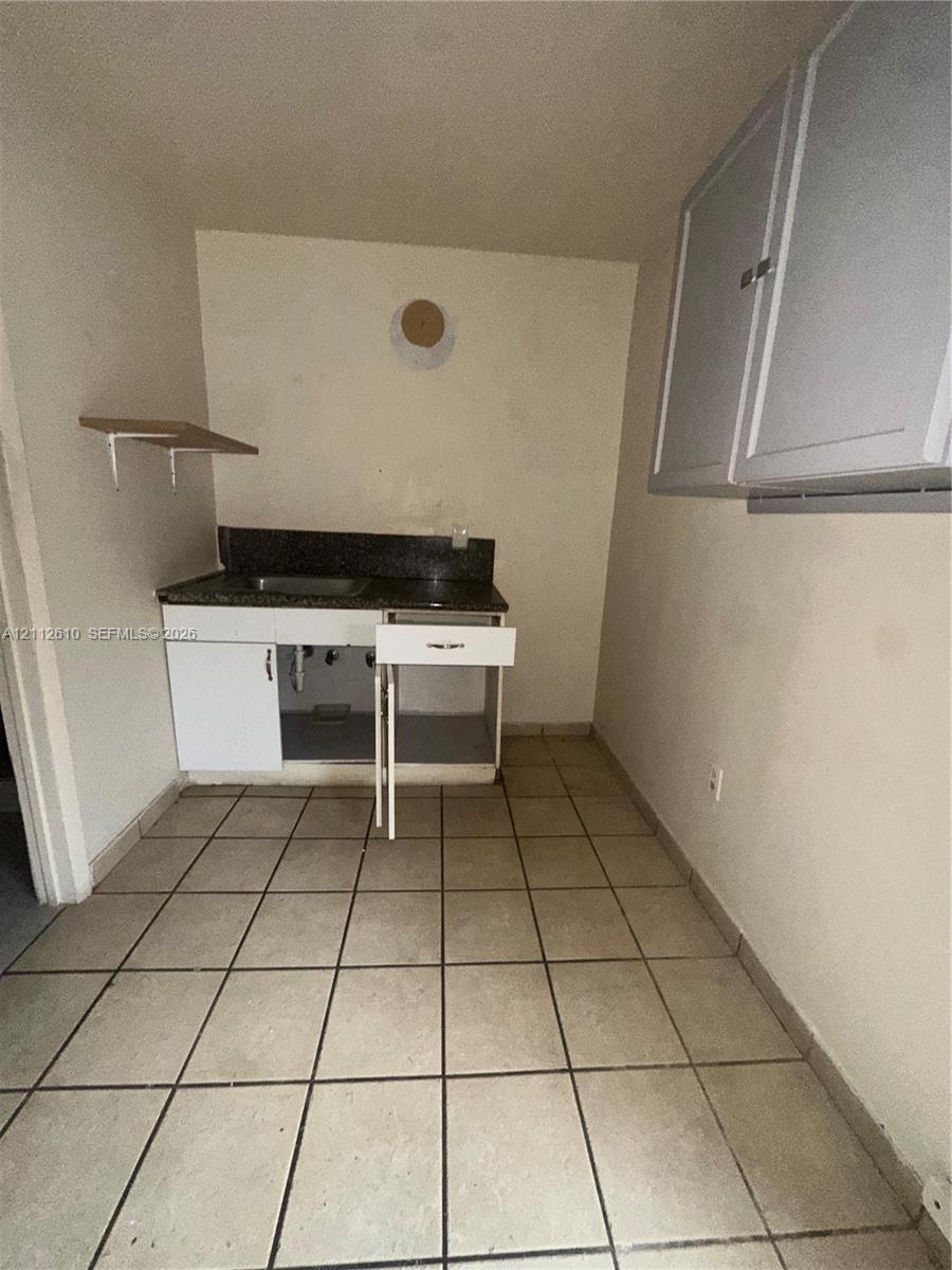 Kitchenette featuring a stone-finish countertop, stainless steel sink, lower cabinetry with integrated drawer, wall-mounted upper cabinetry, and ceramic tile flooring