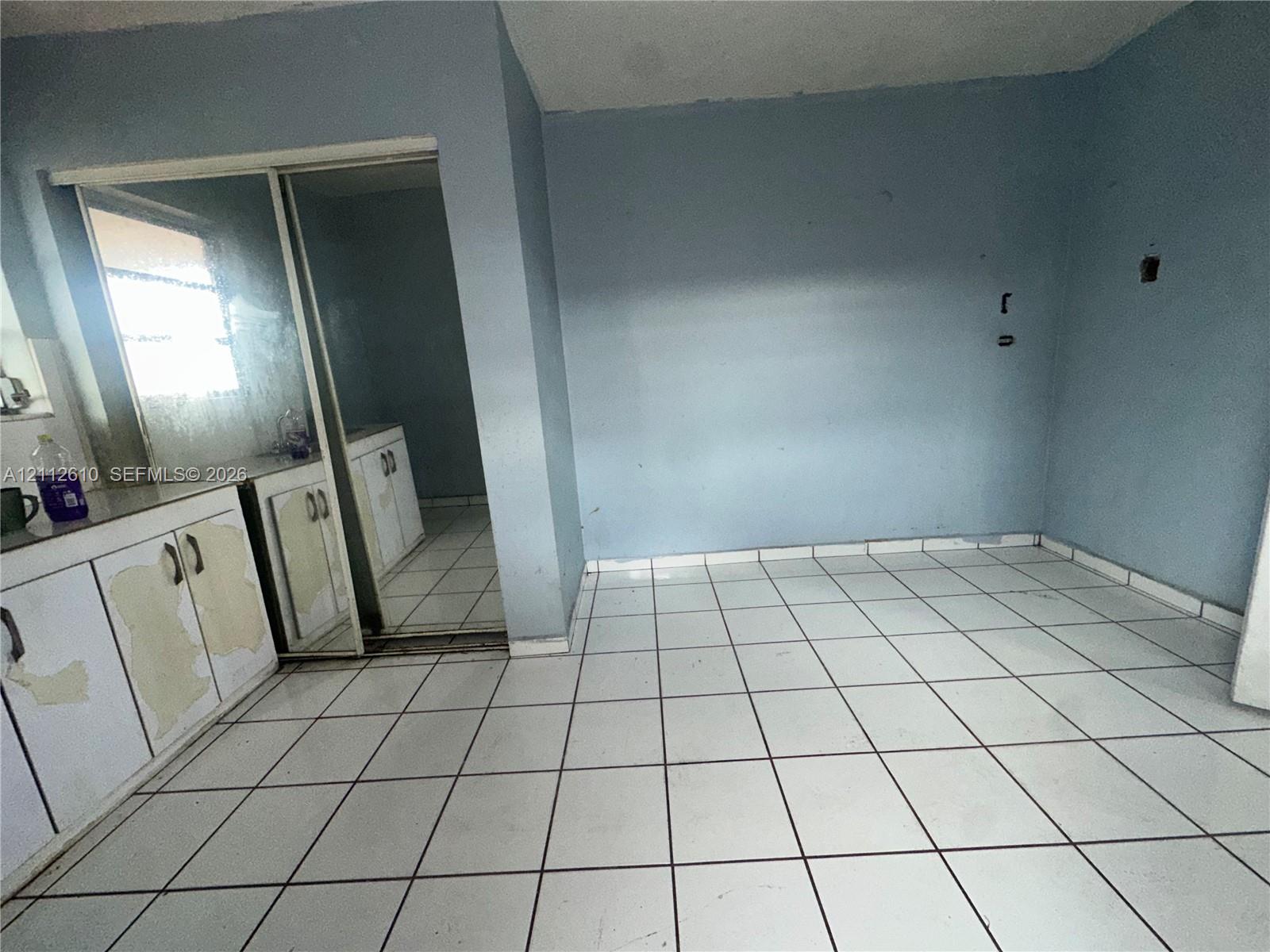 Room interior featuring white tile flooring, built-in cabinetry with hardware, and sliding mirrored closet doors