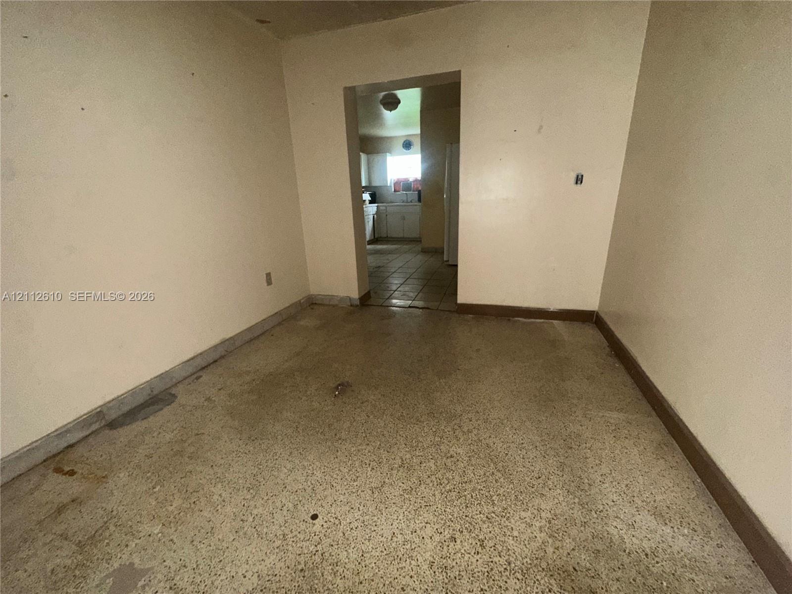 Interior space featuring terrazzo flooring and a threshold leading to a secondary room with tiled flooring and white cabinetry