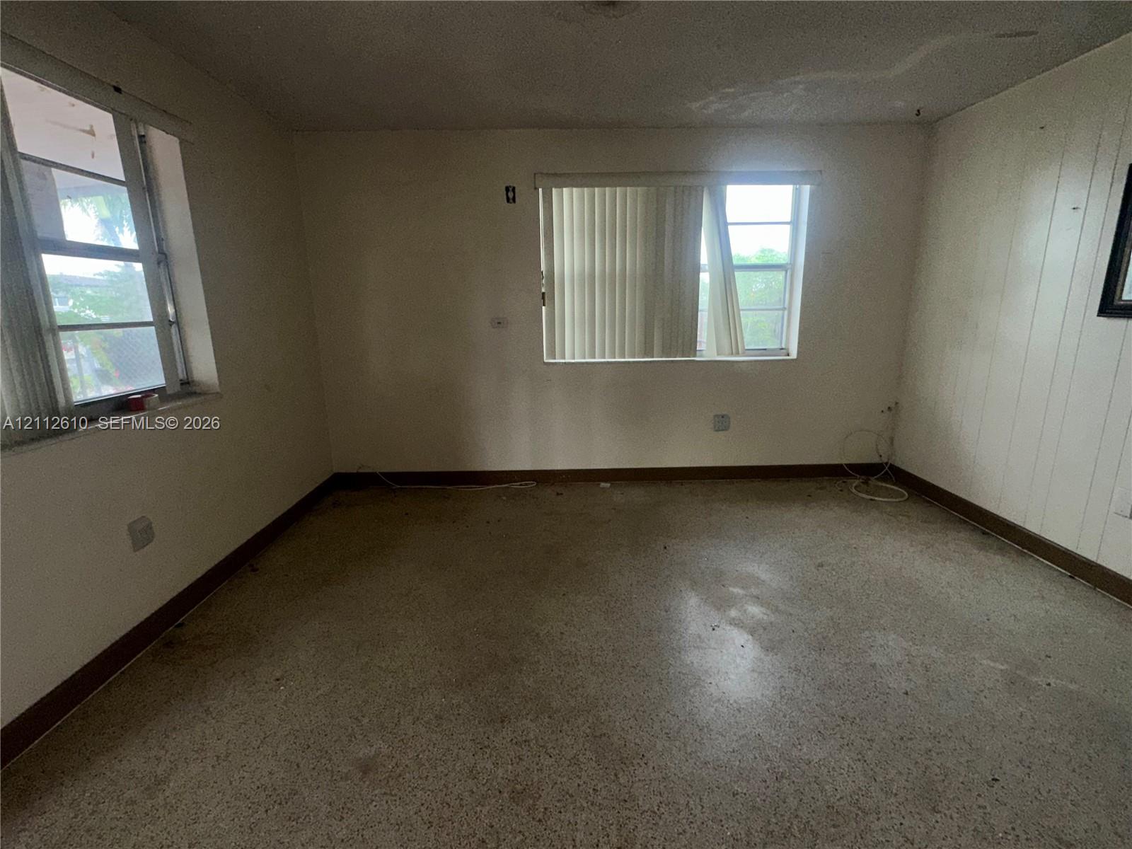 Interior space featuring terrazzo flooring, paneling on one wall, and two windows with horizontal blinds
