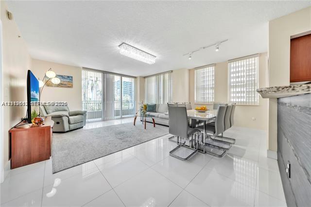 Open-concept living space featuring high-gloss tile flooring, floor-to-ceiling glass doors, built-in breakfast bar, contemporary crystal chandelier, and track lighting
