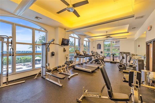 Fitness center featuring expansive floor-to-ceiling windows, tray ceilings with recessed lighting, and industrial ceiling fans