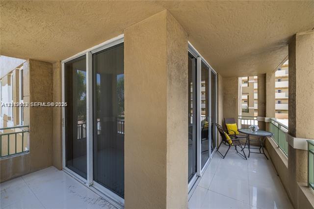 Covered balcony featuring white tiled flooring, stucco walls, dual sliding glass door access, and green metal railings