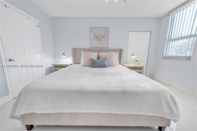 Bedroom featuring white tile flooring, vertical window blinds, and dual interior paneled doors