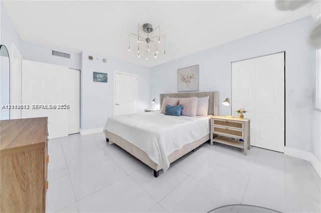Spacious room featuring glossy tile flooring, dual closets with bi-fold doors, and a decorative multi-arm chandelier
